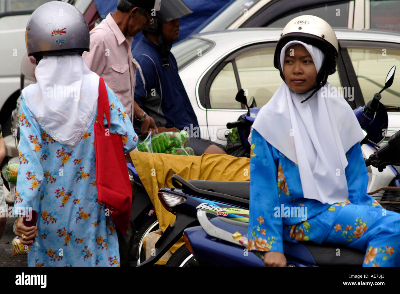 Muslimische Frauen mit Motorradhelme über traditionelle Kopf bedecken außerhalb des Marktes, Kuching, Sarawak, Borneo, Malaysia Stockfoto