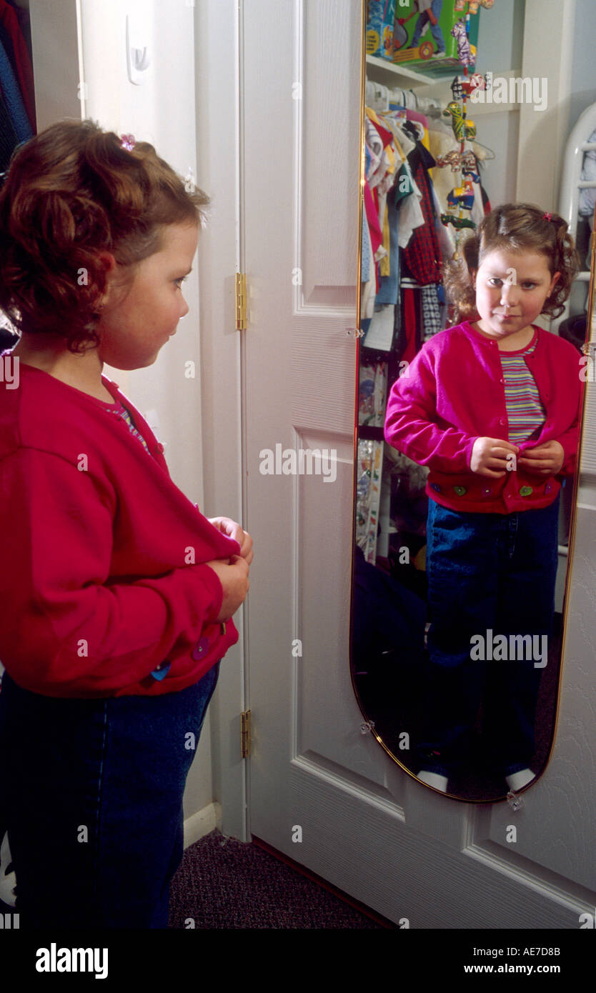 Fünf Jahre alten Mädchen immer gekleidet betrachtet sich im Spiegel Stockfoto