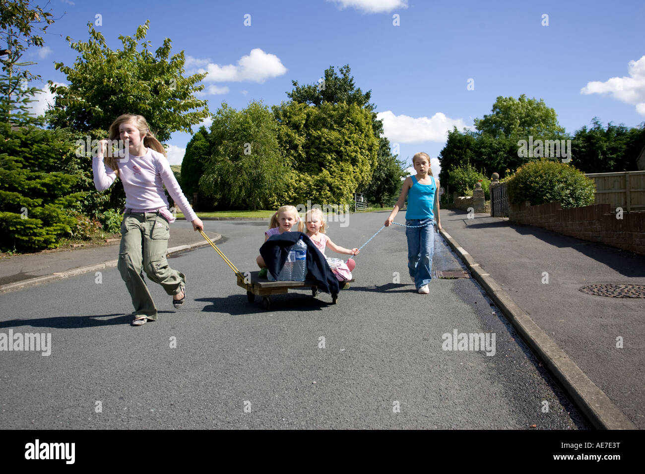 Mädchen, die Spaß ziehen jüngere Schwestern entlang ruhigen Straße am hausgemachten trolley UK Stockfoto