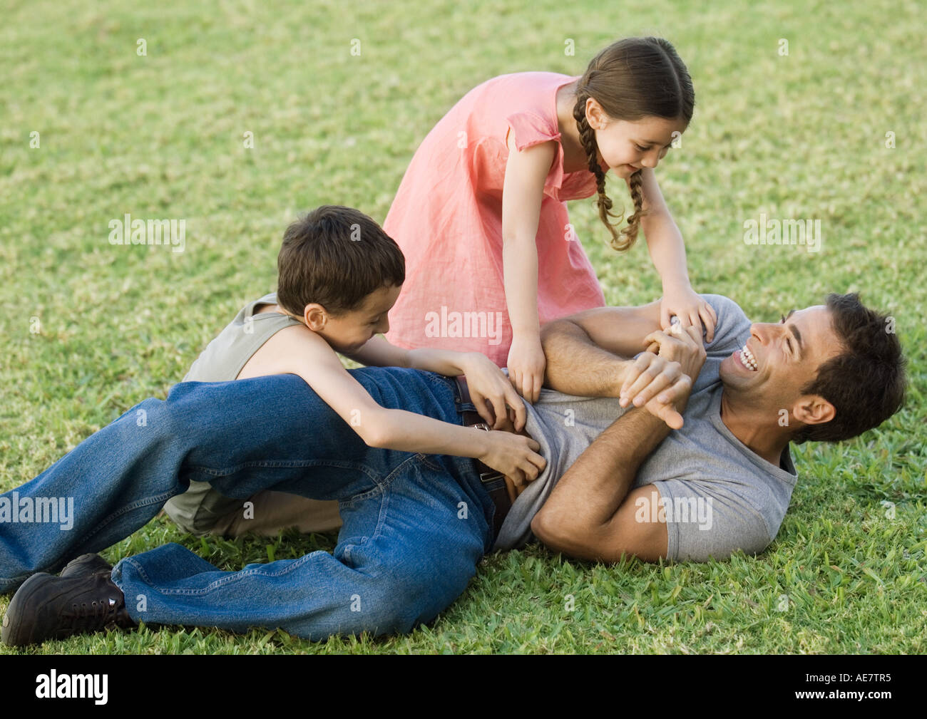 Jungen und Mädchen kitzeln Vater auf Rasen Stockfoto