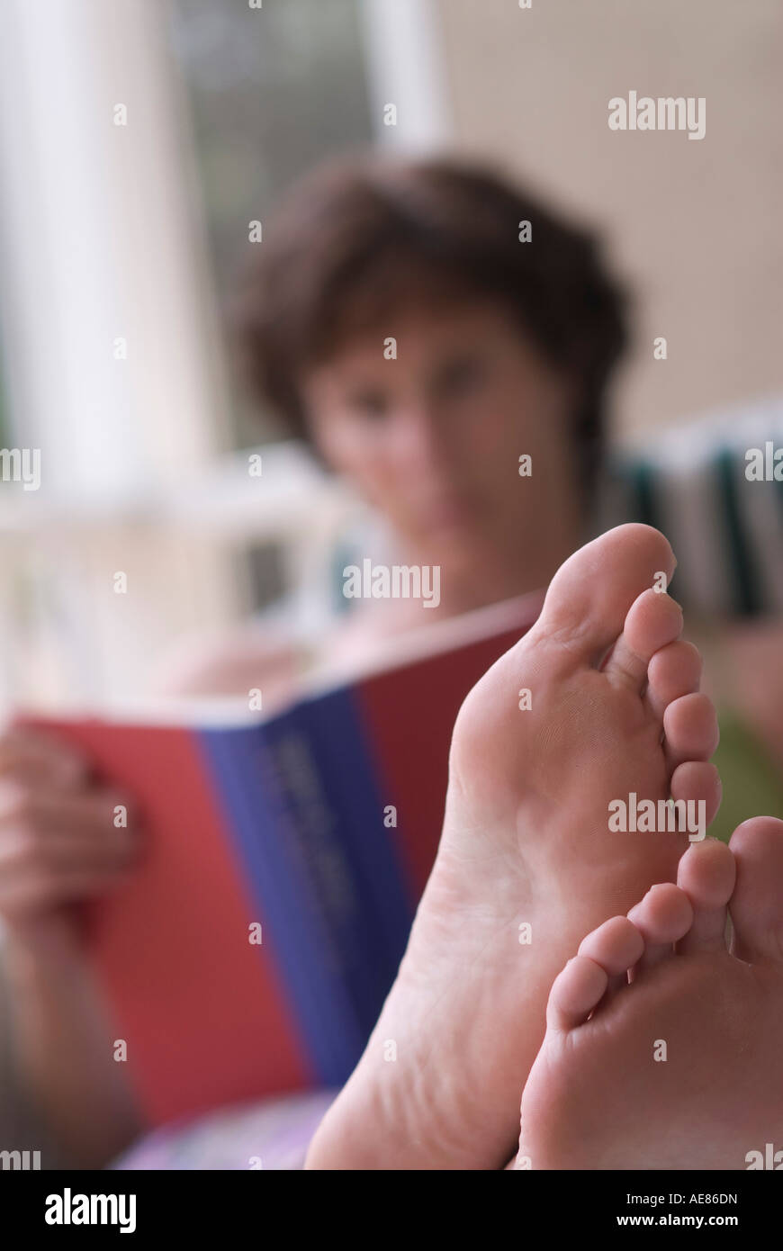 Nahaufnahme einer barfuß Frau, ein Buch zu lesen, während Sie sitzen auf einer Couch mit ihren Füßen Stockfoto