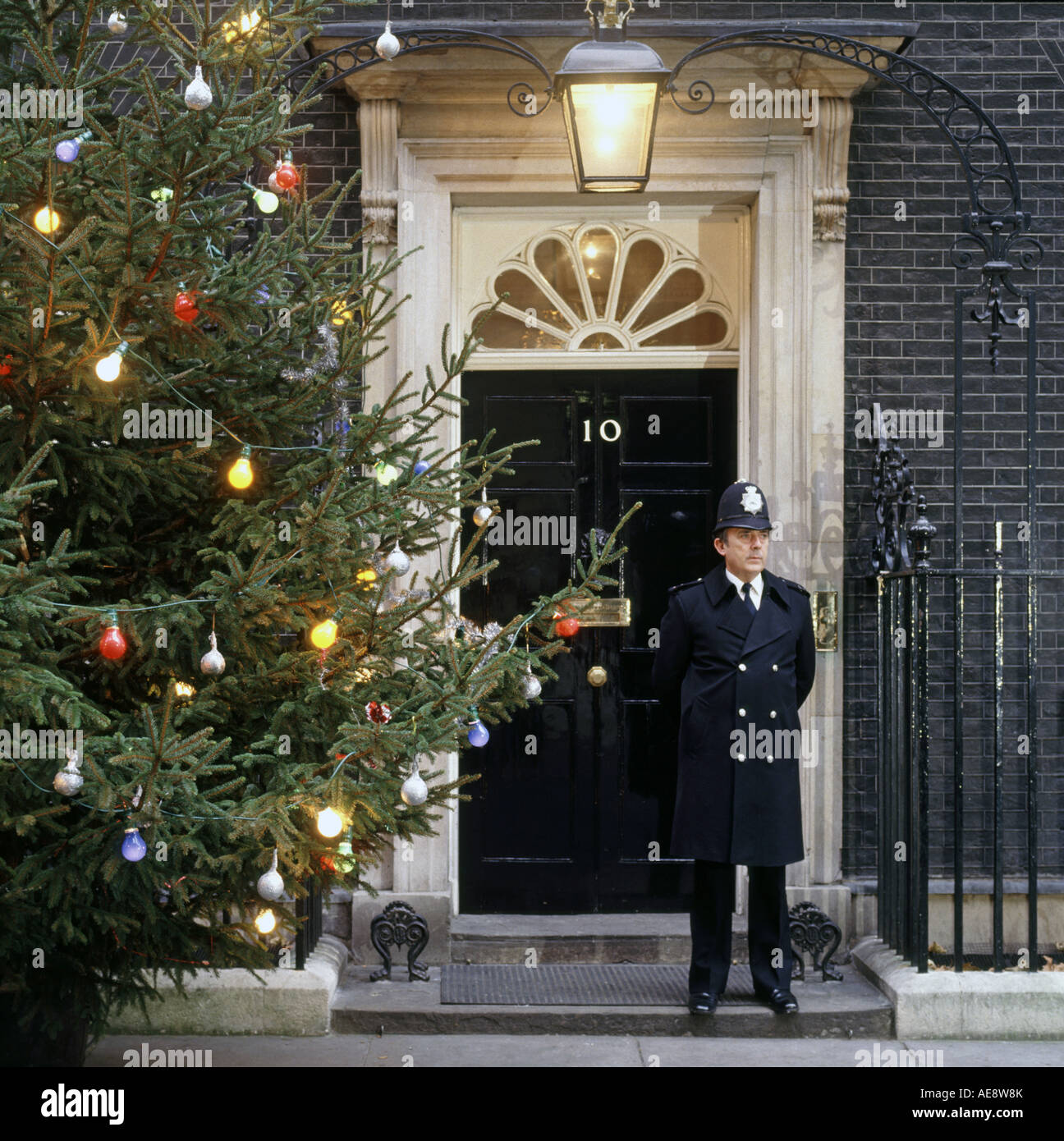 Metropolitan Police Officer Nachtdienst steht vor der berühmten Eingangstür der Nr. Ten 10 Downing Street neben beleuchtetem Weihnachtsbaum UK Stockfoto