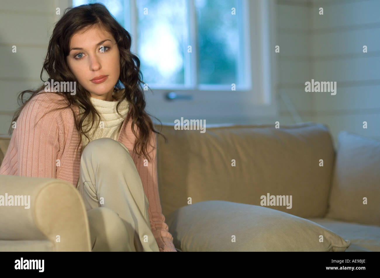 Junge Frau sitzt auf dem Sofa, schaut in die Kamera Stockfoto
