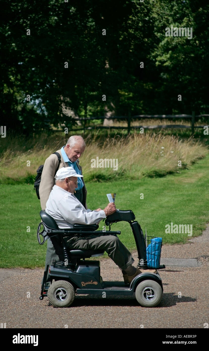 Zwei ältere Männer, einer auf einem Motorroller, der im Sommer einen englischen Garten besucht Stockfoto