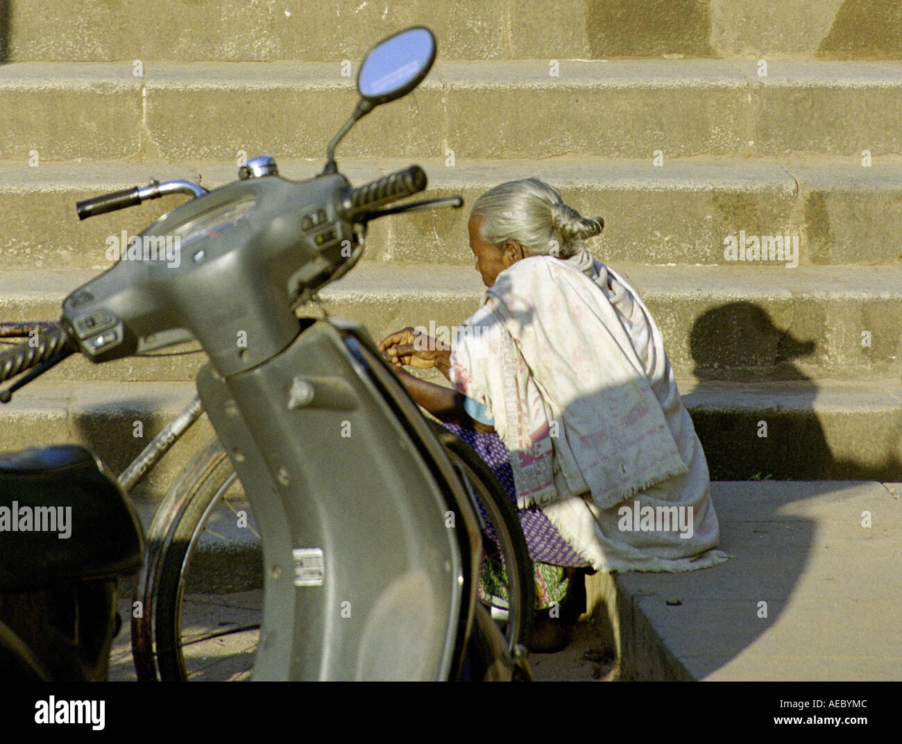 ein geparktes Motorrad und eine sitzende alte Dame mit alten Schritte im Hintergrund Stockfoto