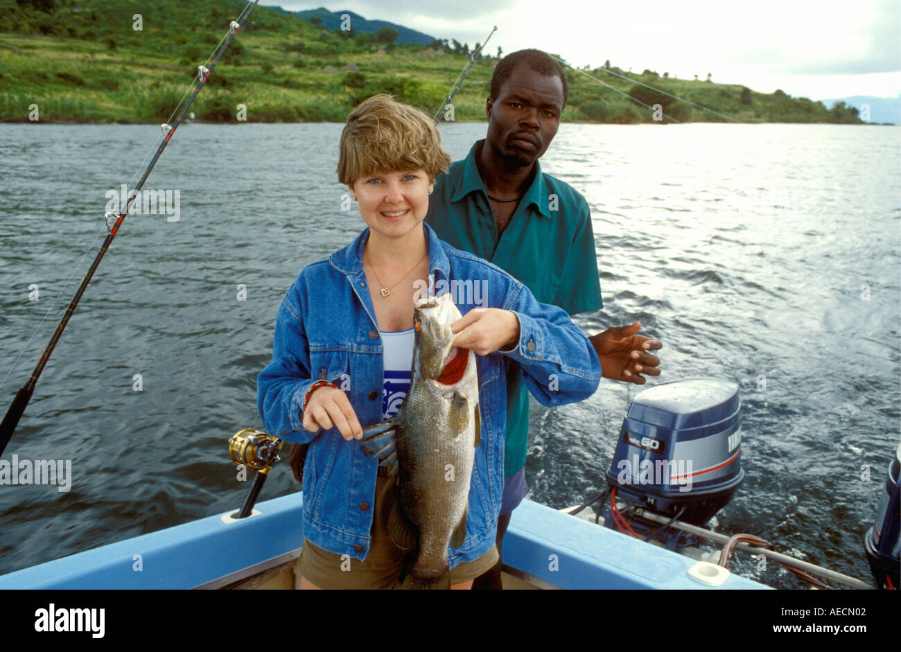Hübsche junge weiße Frau mit Nilbarsch gefangen am Viktoriasee Kenia in Ostafrika die schwarzen Afrika Boatman hinter ihr ist Stockfoto