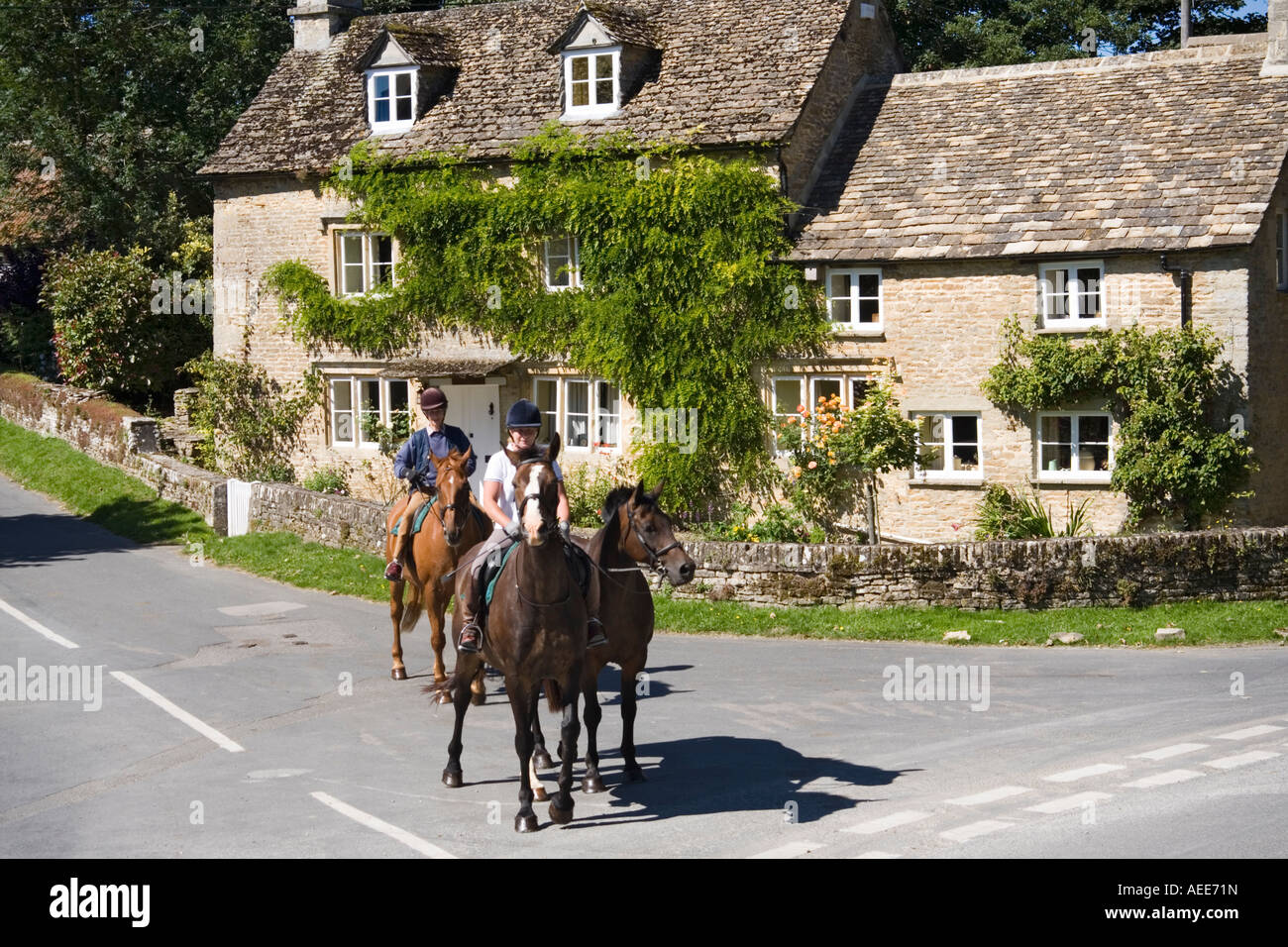 Pferdereiten passieren ein Steinhaus im Dorf Cotswold Eastleach Turville, Gloucestershire, Großbritannien Stockfoto