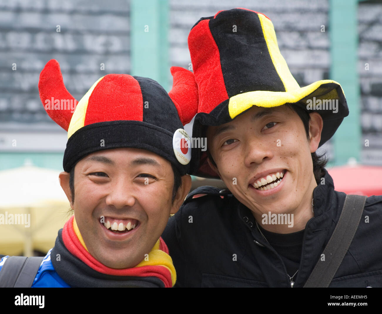 Zwei japanische Fußballfans gut gelaunt posieren mit Hüten in deutschen Nationalfarben Stockfoto