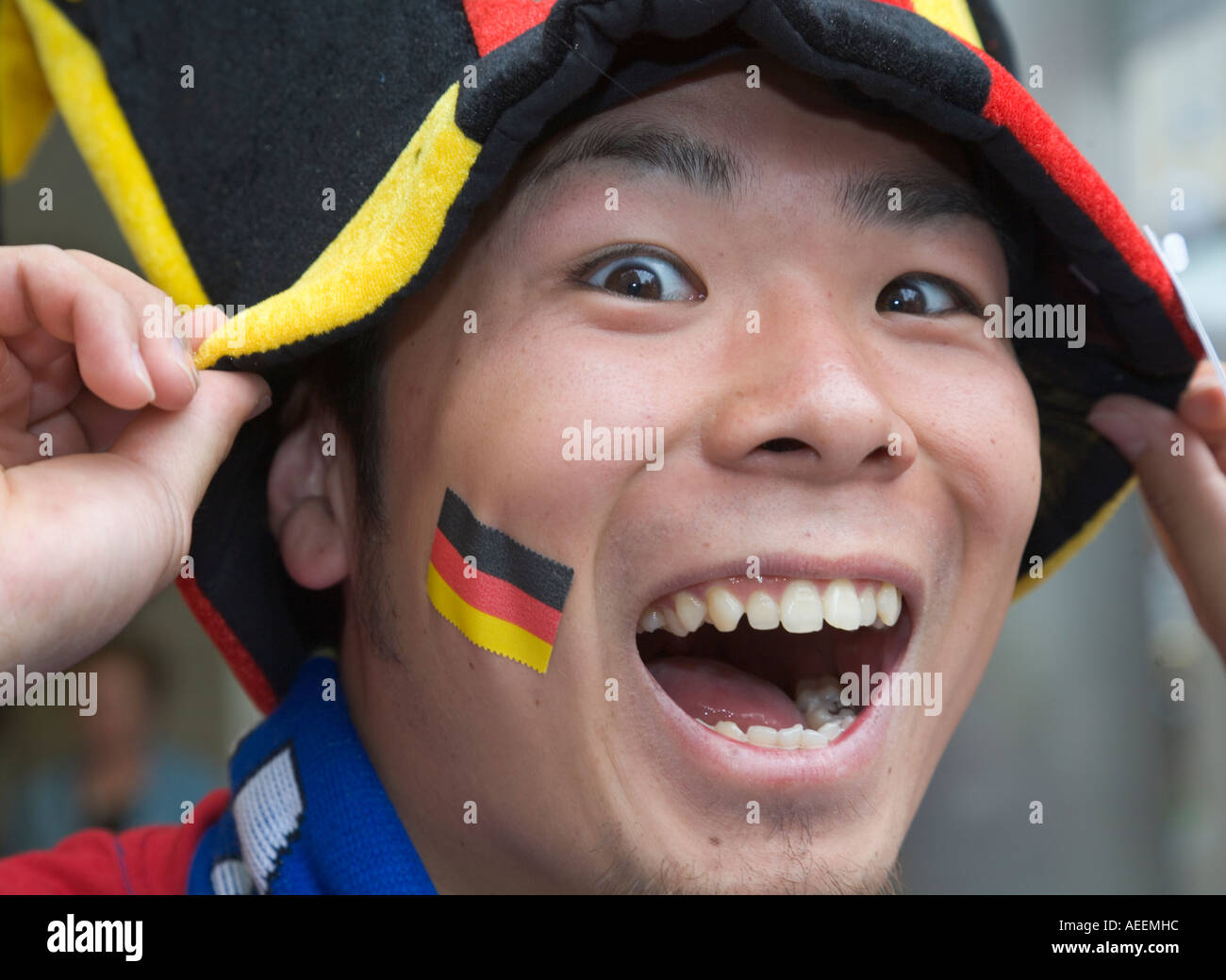 Ein japanischer Fußball-Fan gut gelaunt posieren mit Hut und Aufkleber in deutschen Nationalfarben Stockfoto