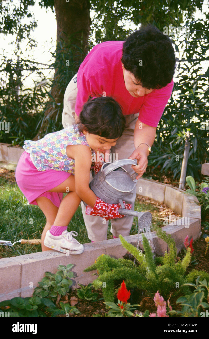 Hispanic Mama Mädchen 4-5 Jahre Jahre alten Bewässerung besprüht kann Besprengung Pflanzen Hintergrund Sommerabend POV Kaukasischen HERR © Myrleen Pearson Stockfoto