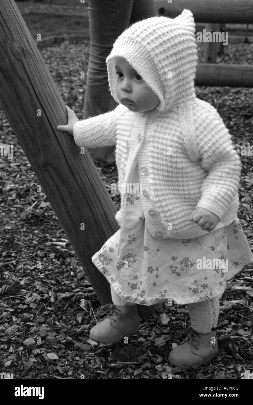 Kleinkind Tragen eines weißen Strickjacke toddling und halten auf einen Holzbalken Stockfoto