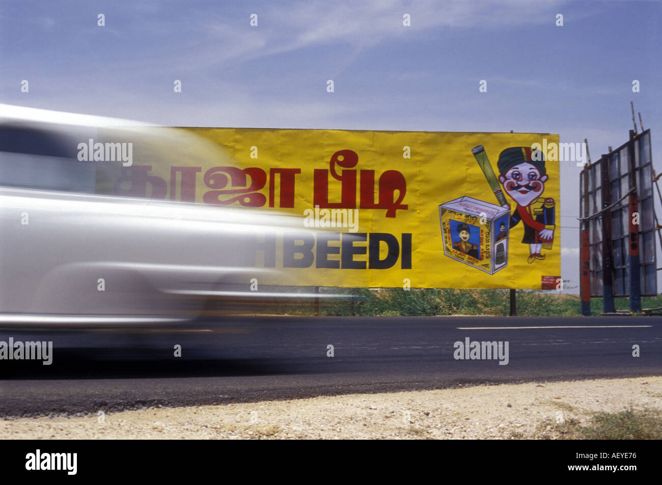 Eine Botschafter Auto beschleunigt vorbei an einem Straßenrand Billboard Werbung Zigaretten in Tamil Nadu Indien Bild von Andrew Hasson 2002 Stockfoto