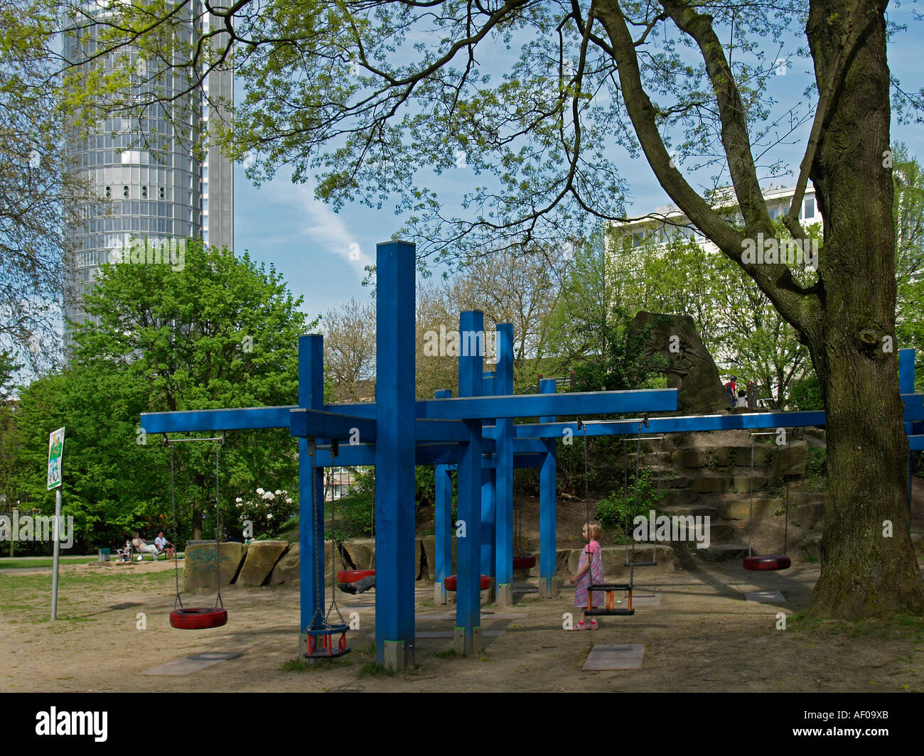 schwingt sich auf den Kinderspielplatz im Stadtgarten in Essen RWE-Turm im Hintergrund Stockfoto
