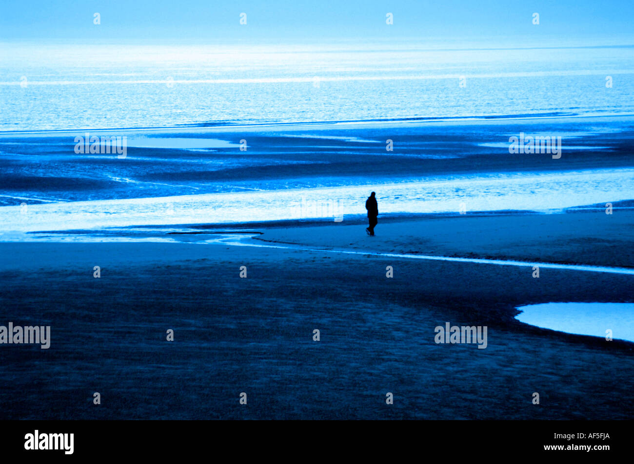 einsamer Mensch allein zu Fuß entlang Strand Kältegefühl kalte blaue Farbe Winter einzelne isolierte Strand Meer Sand Wasser Stockfoto