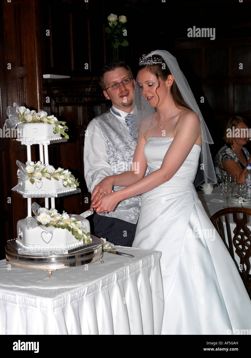 Braut und Bräutigam schneiden den Kuchen an der Hochzeit Empfang in England Stockfoto