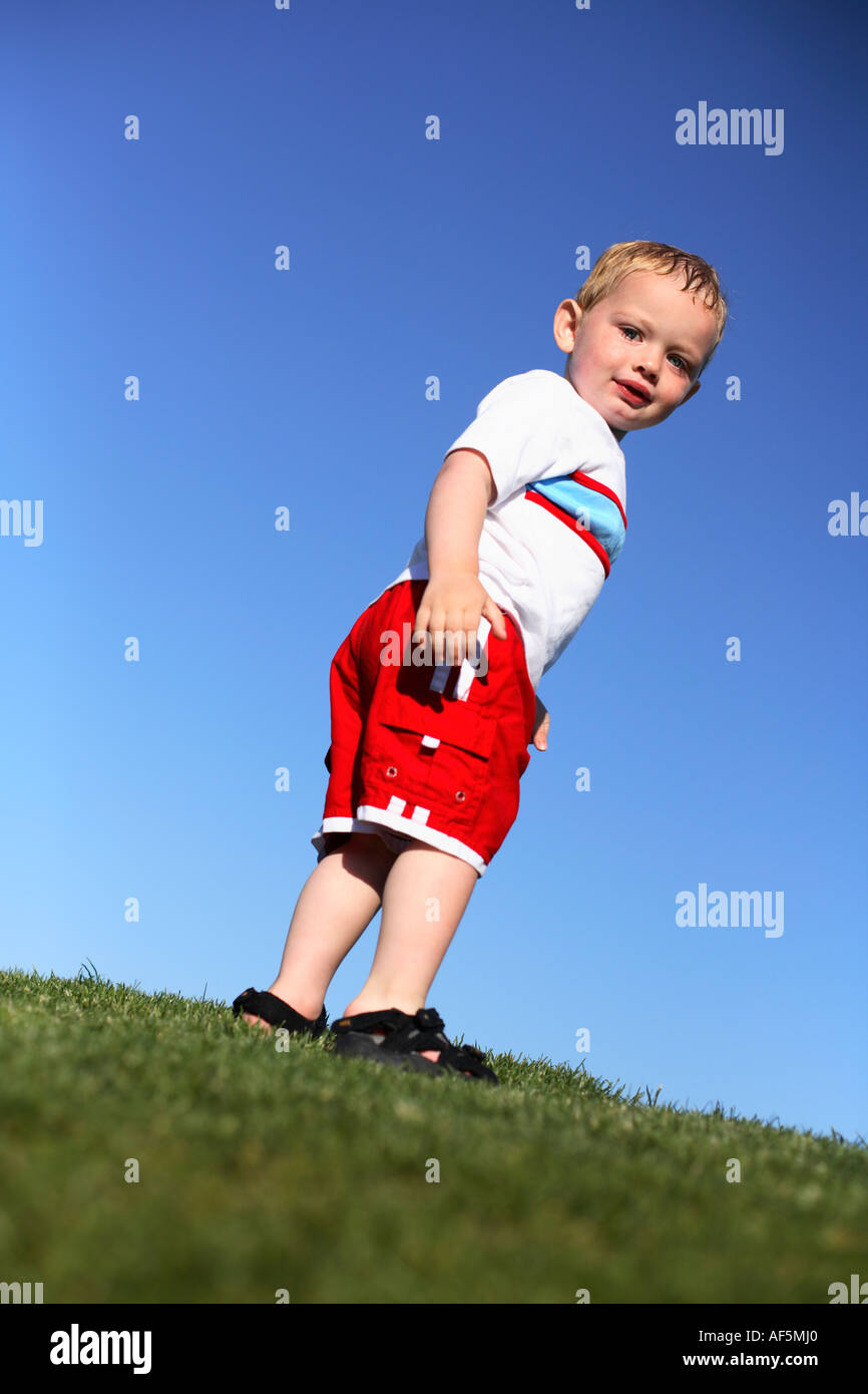 Zwei Jahre alte Junge stand auf dem Rasen drehen, um in die Kamera schauen. Stockfoto