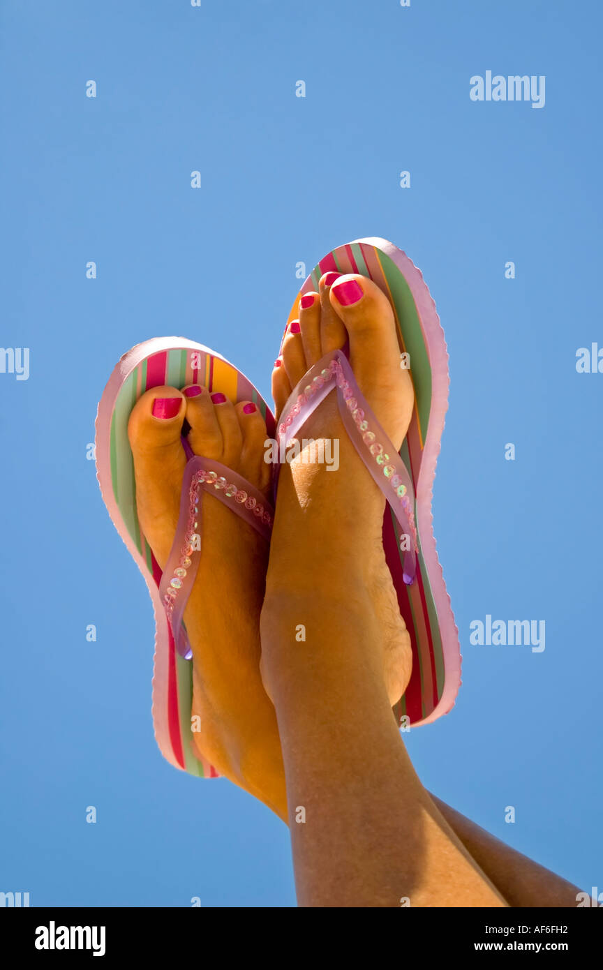 Vertikale Nahaufnahme von einer Frau gebräunte Füße mit lackierten Zehennägeln tragen gestreifte gegen ein strahlend blauer Himmel Flipflops Stockfoto