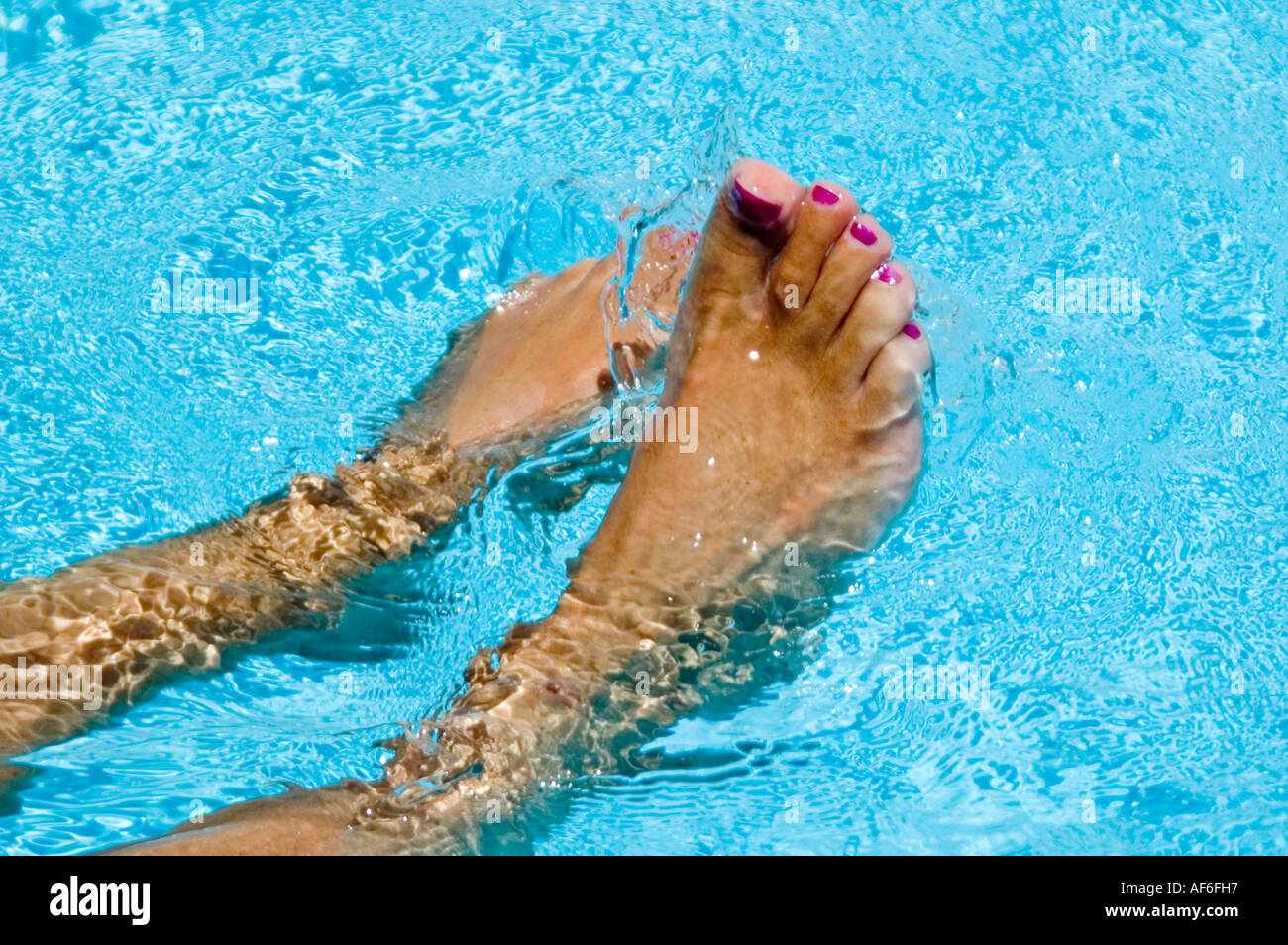 Horizontale Nahaufnahme von gebräunte nasse Füße mit lackierten Zehennägeln in einem leuchtend blauen Pool plantschen Stockfoto