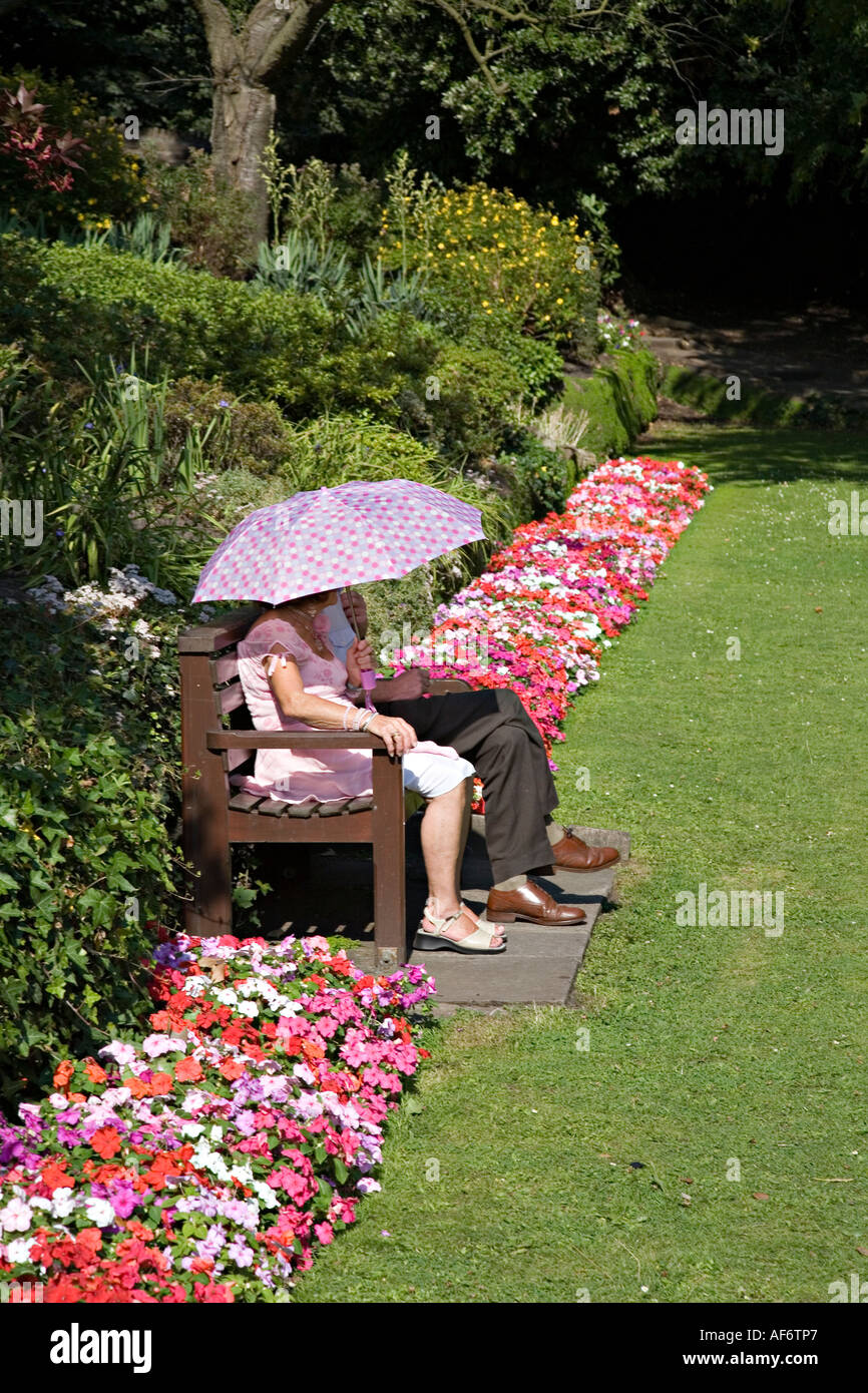 Mann und Frau mit Sonnenschirm in Sommersonne sitzen in öffentlichen Gärten Abergavenny Wales UK Stockfoto