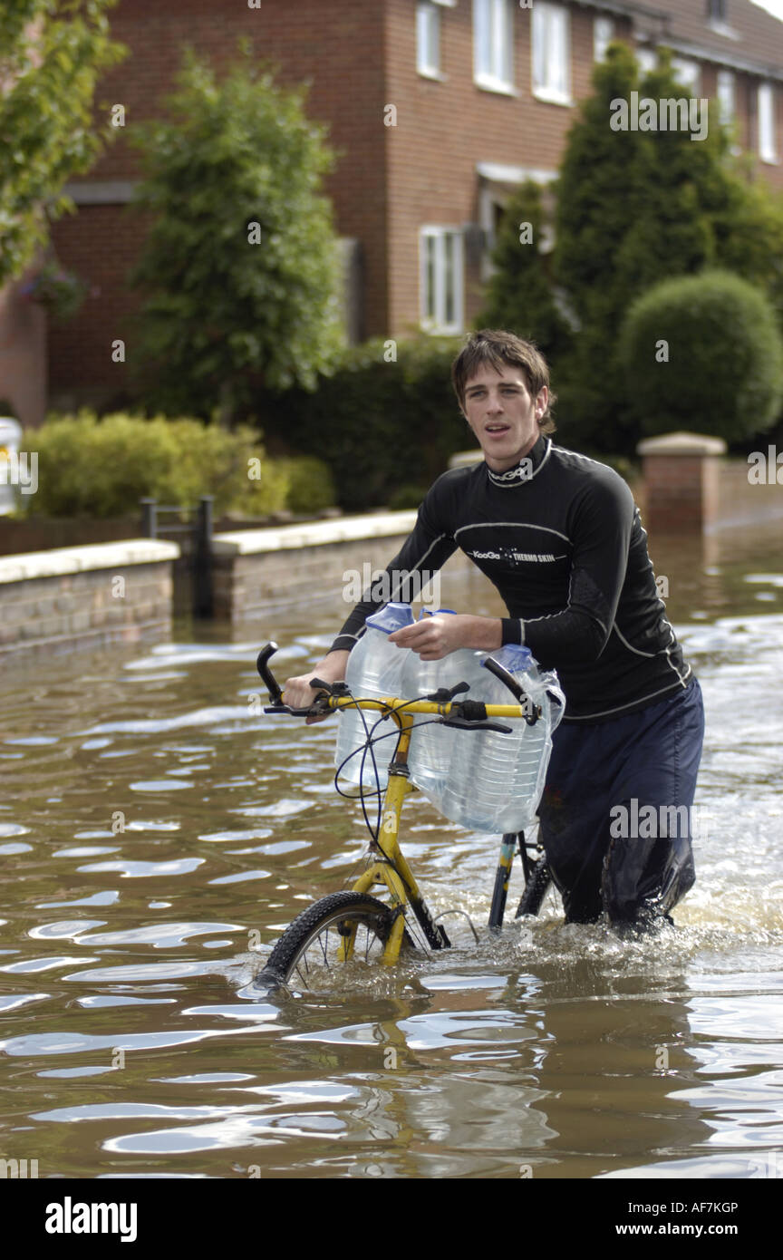 Mann trägt Mineralwasser auf seinem Fahrrad in den Fluten im Bereich Longlevens von Gloucester in England im Juli 2007 Stockfoto