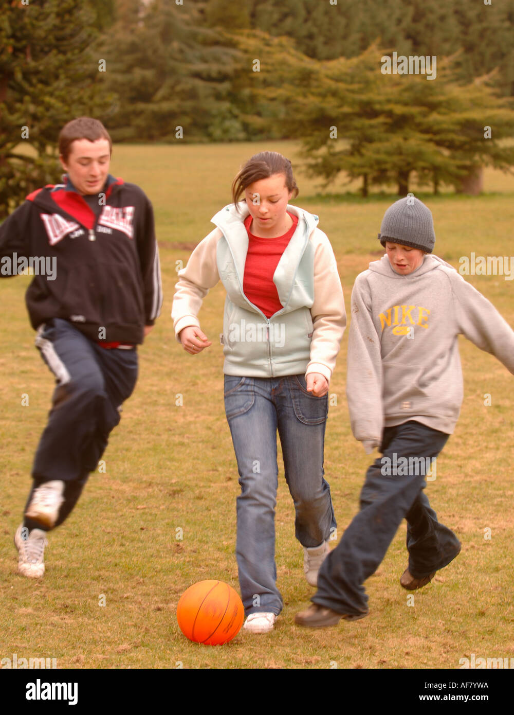 EINE GRUPPE VON TEENAGER-JUNGEN UND MÄDCHEN SPIELEN FUßBALL IN EINEM PARK UK Stockfoto