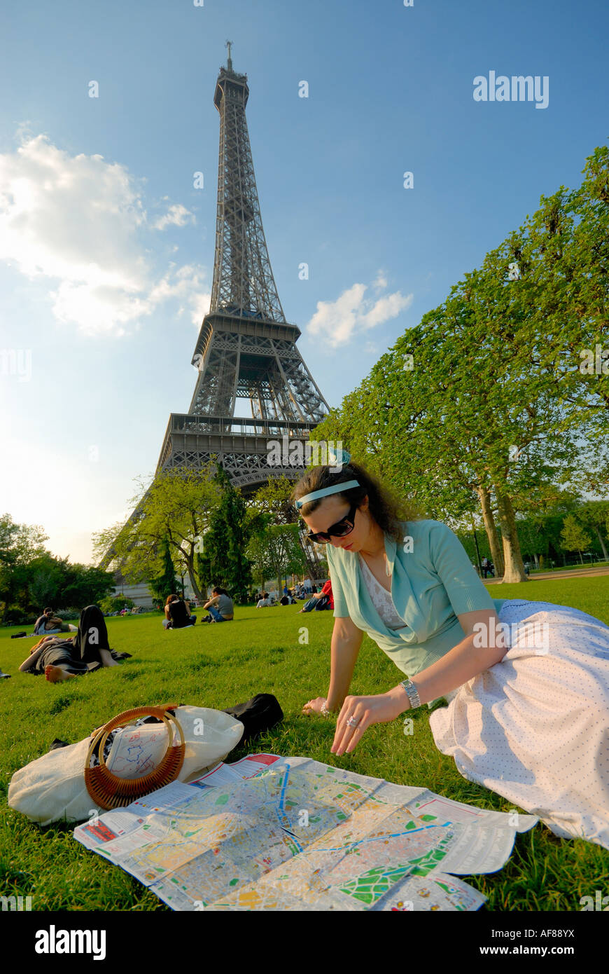 junge Frau mit Touristenkarte sitzen auf Rasen mit Eiffelturm hinter Paris Frankreich Stockfoto