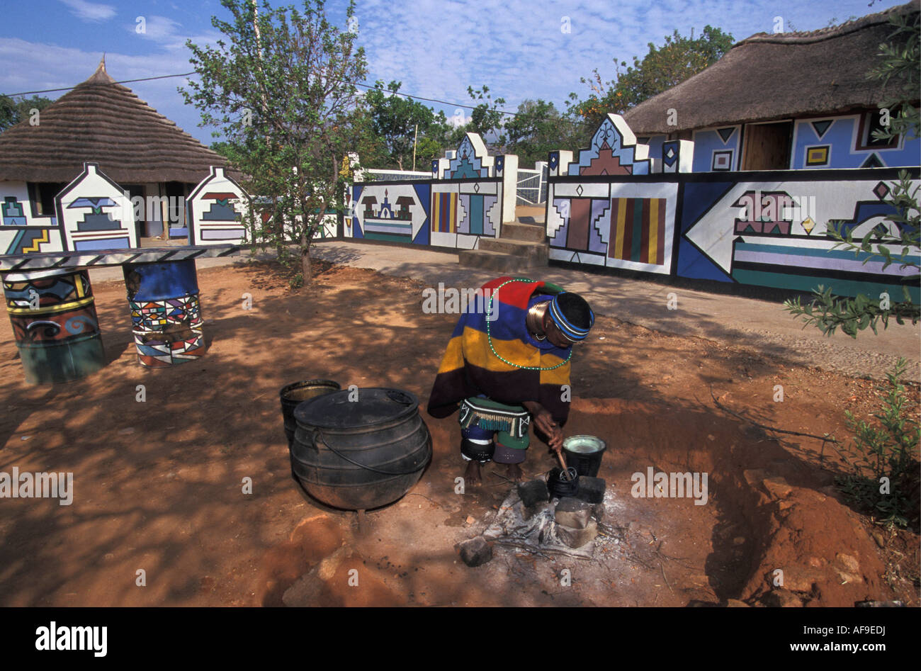 Südafrika Mapoch Ndebele Dorf in der Nähe von Pretoria Frau kochen Häusern mit traditionellen Wandmalereien im Hintergrund. Stockfoto