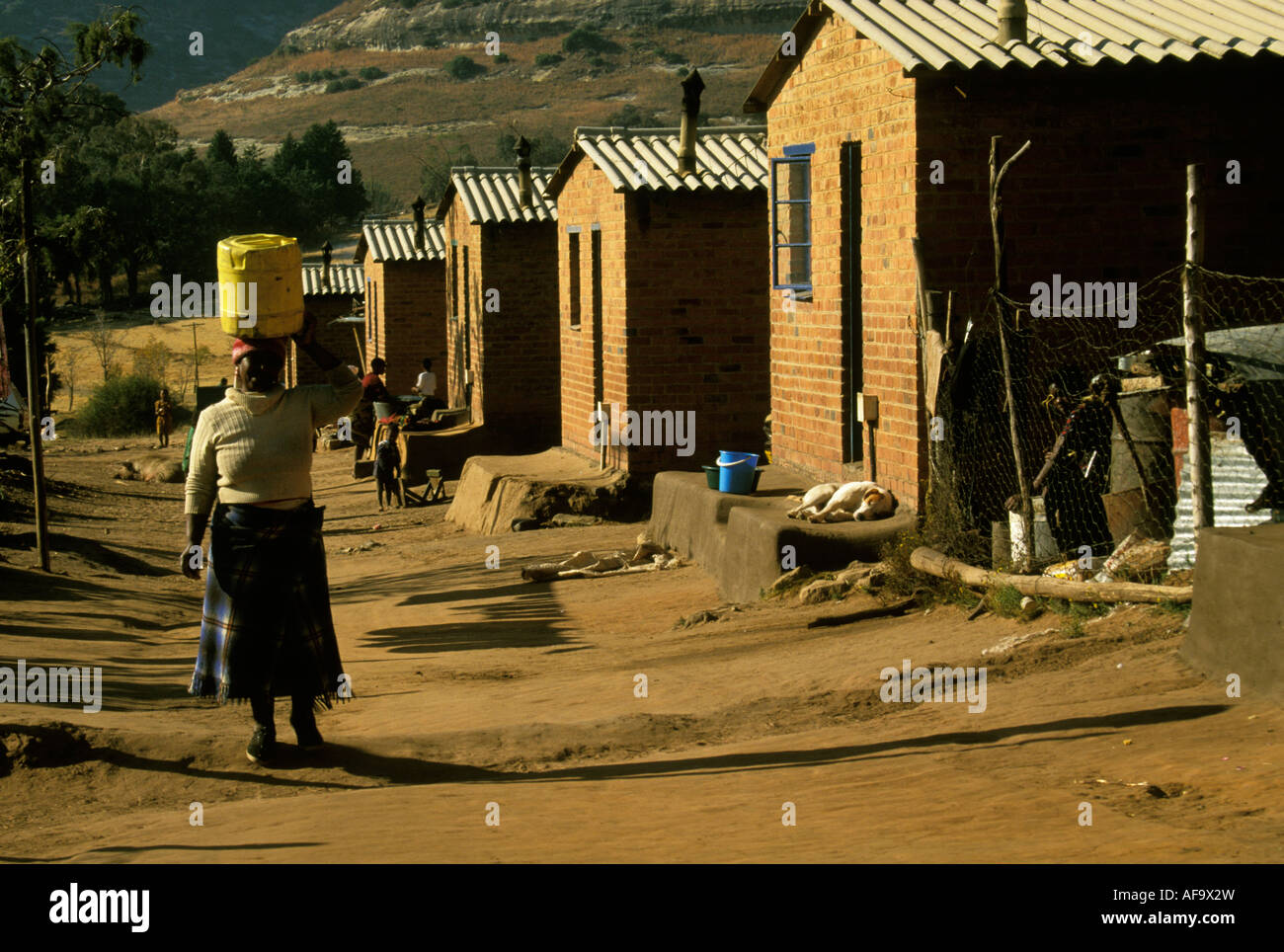 Eine Frau, die zu Fuß durch eine ländliche Siedlung, die mit Wasser gefüllten Trommel auf dem Kopf Lesotho Stockfoto