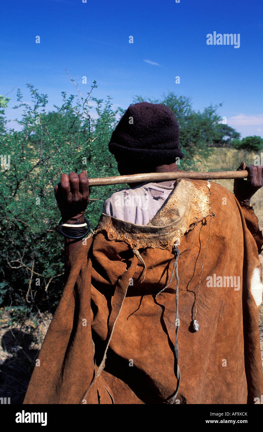 Kua Buschmann Frau zu Fuß auf der Suche nach Nahrung mit Stick über Schultern in die Kalahari Wüste zu graben. Stockfoto