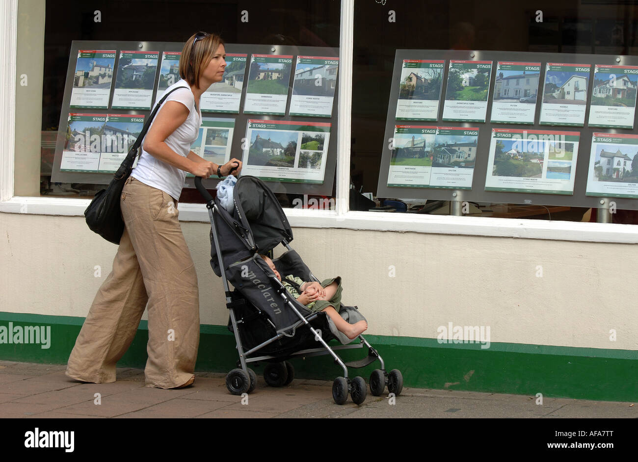 Eine Mutter mit ihrem Kind im Kinderwagen suchen Sie im Fenster ein Immobilienmakler-Büro in Barnstaple, North Devon. Stockfoto