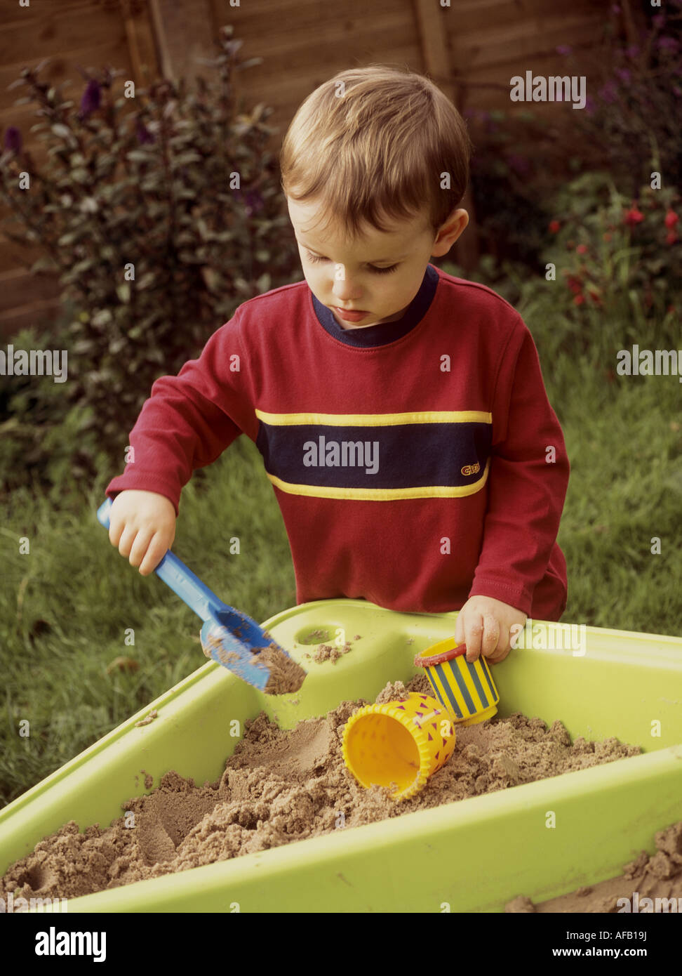 Kleiner Junge spielt mit einem Kunststoff Spaten und Containern in einem Sand Tablett Stockfoto