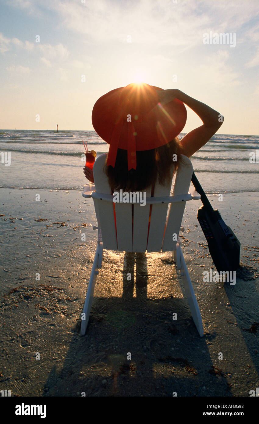 Junge Brünette Frau, die den Sonnenuntergang im Strandkorb hält ein gefrorenes Getränk und eine e-Gitarre auf ihrer rechten Seite Stockfoto