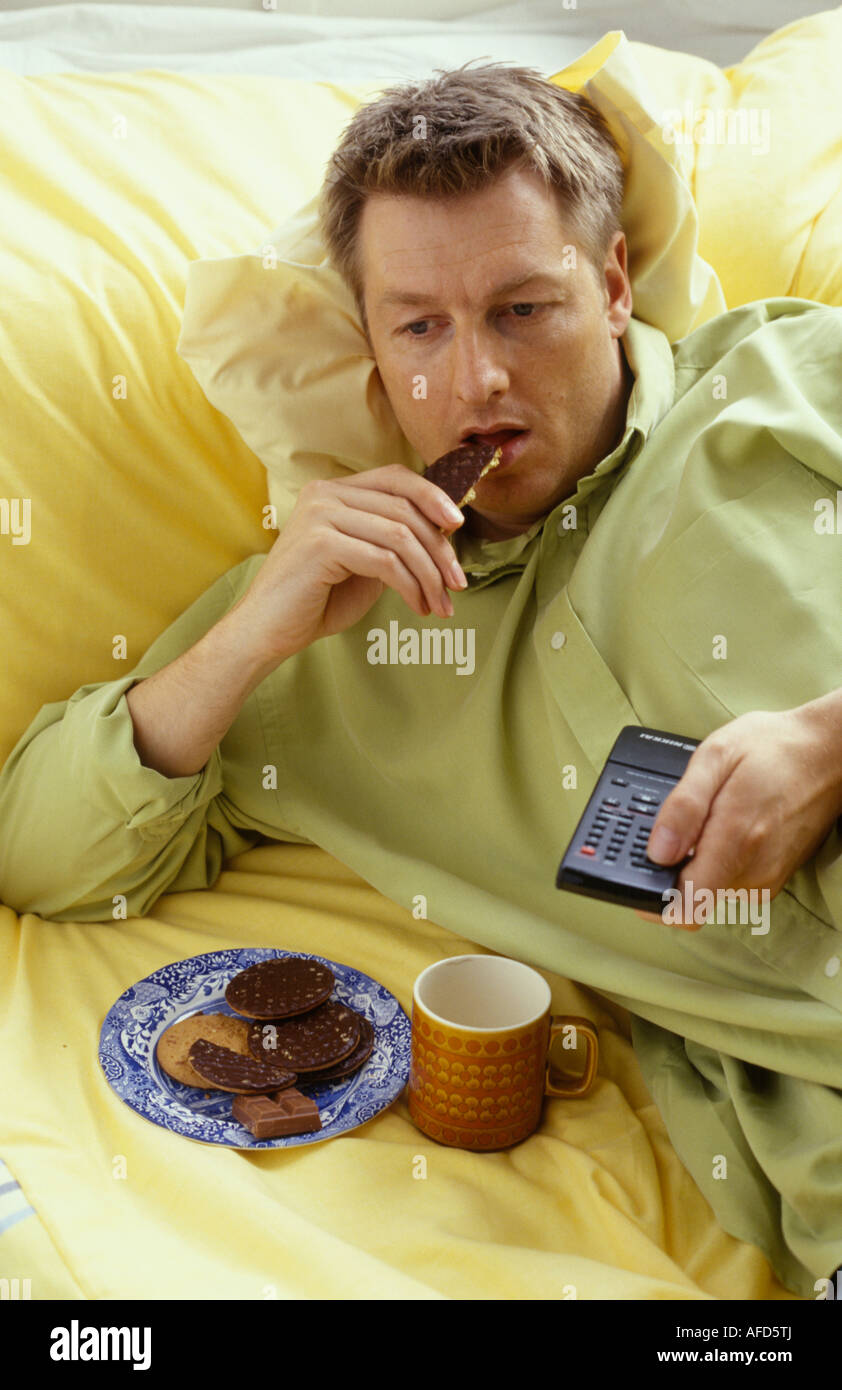 Mann, Kekse essen und trinken Tee vor dem Fernseher Stockfoto