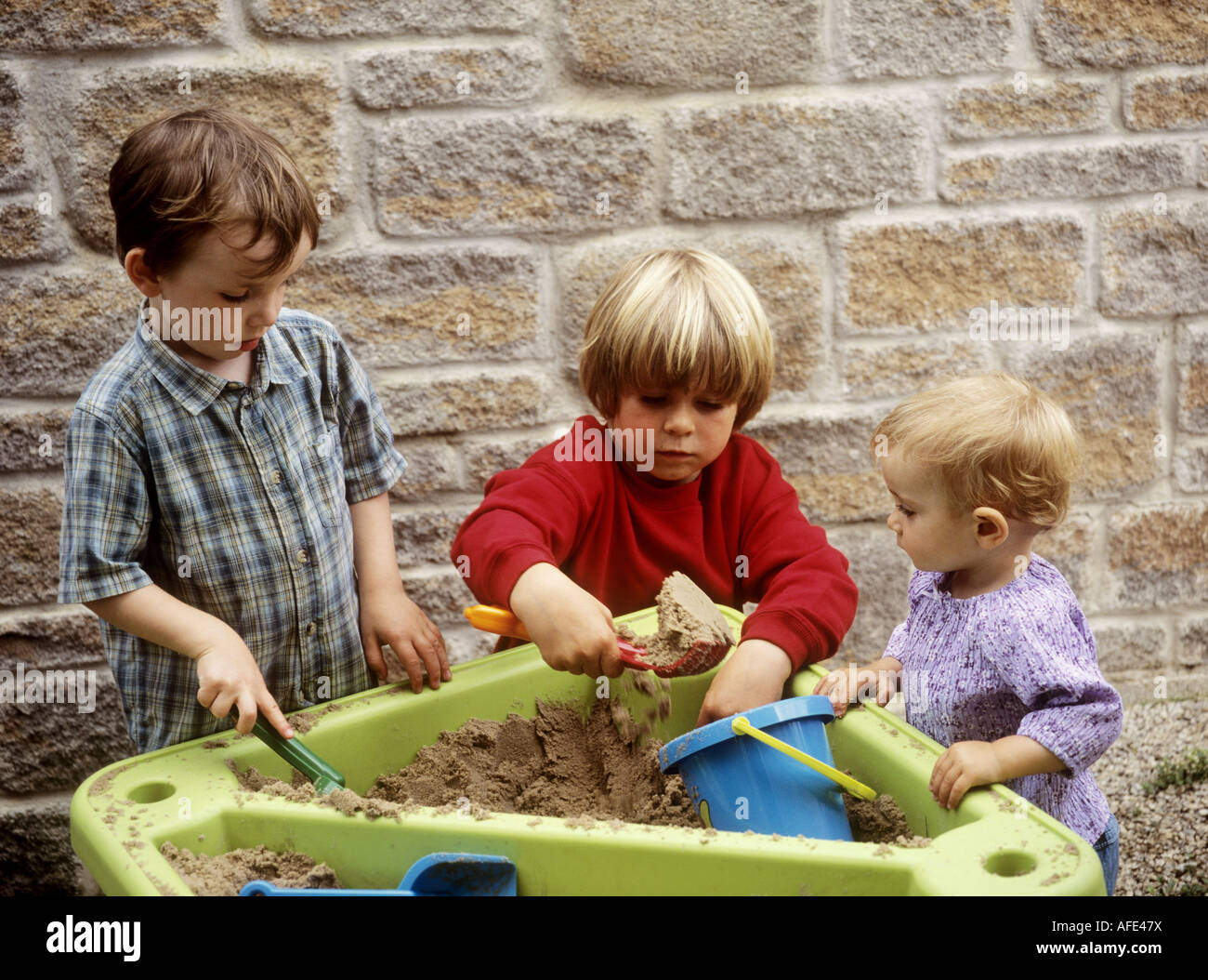 Kleine Kinder spielen mit einem Kunststoff Spaten und Containern in einem Sand Tablett Stockfoto