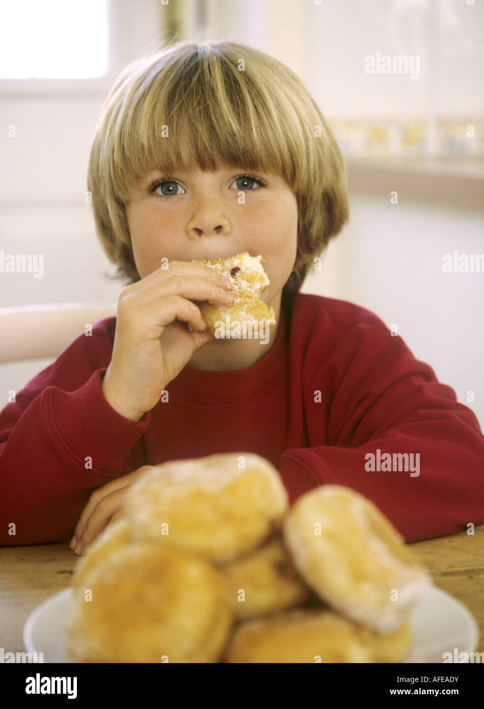 Junge, sitzen an einem Küchentisch essen Donuts Stockfoto