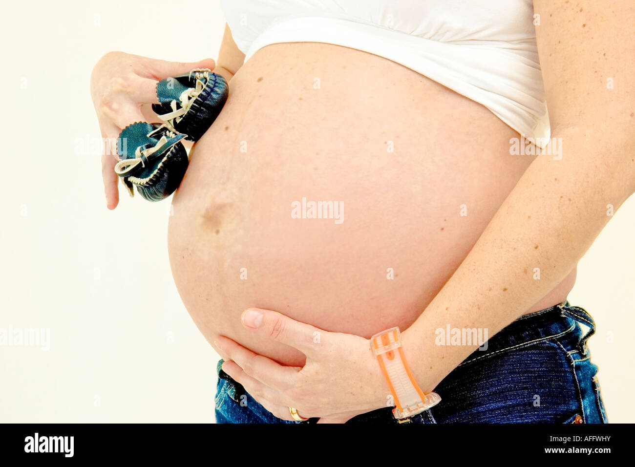 8 Monate schwangere Frau hält ihren Bauch und zwei Baby-Schuhe in ihren Fingern Nahaufnahme Stockfoto