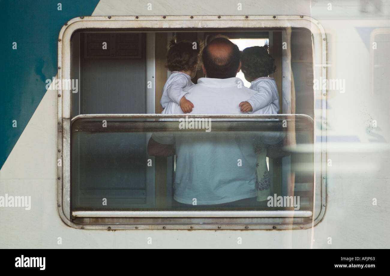 Mann mittleren Alters halten Baby Zwillingsmädchen alle tragen weiße gesehen durch das Fenster ein Personenzug von Trenitalia in Italien Stockfoto