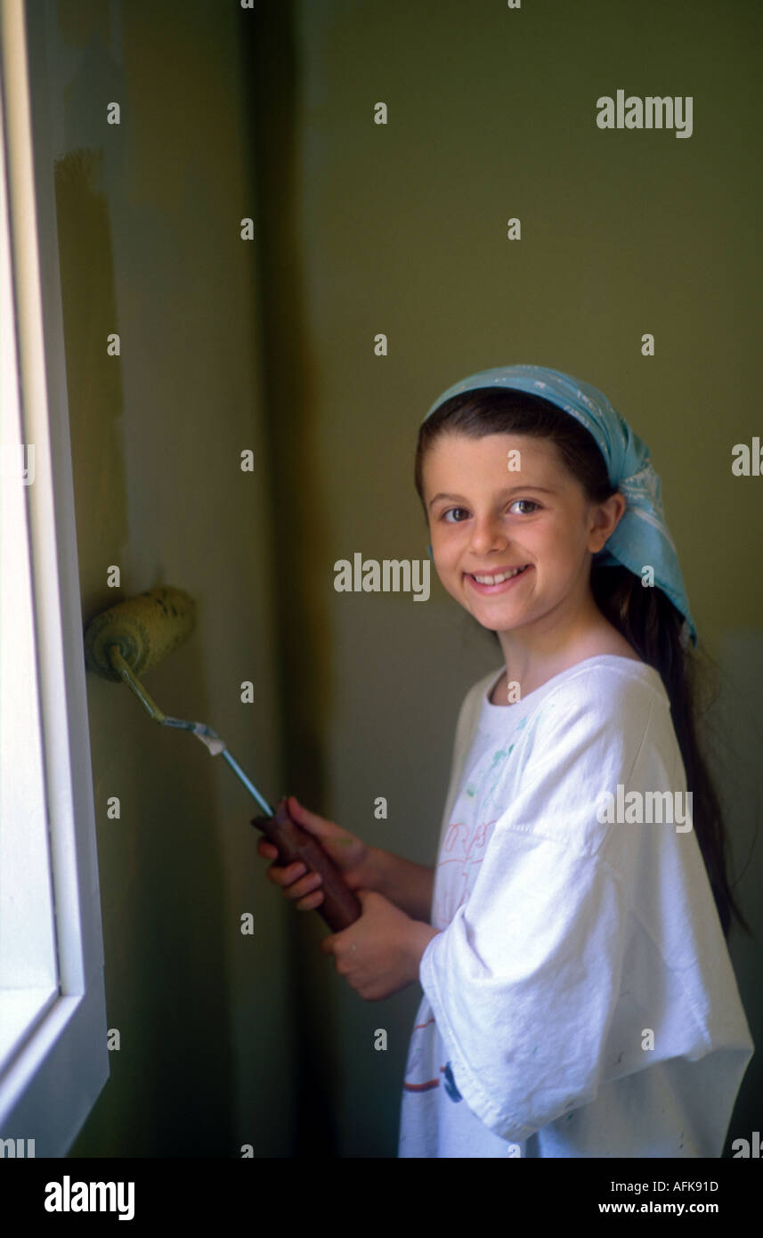 9 Jahre altes Mädchen Malerei Zimmer mit einer Walze in die Kamera Lächeln Stockfoto