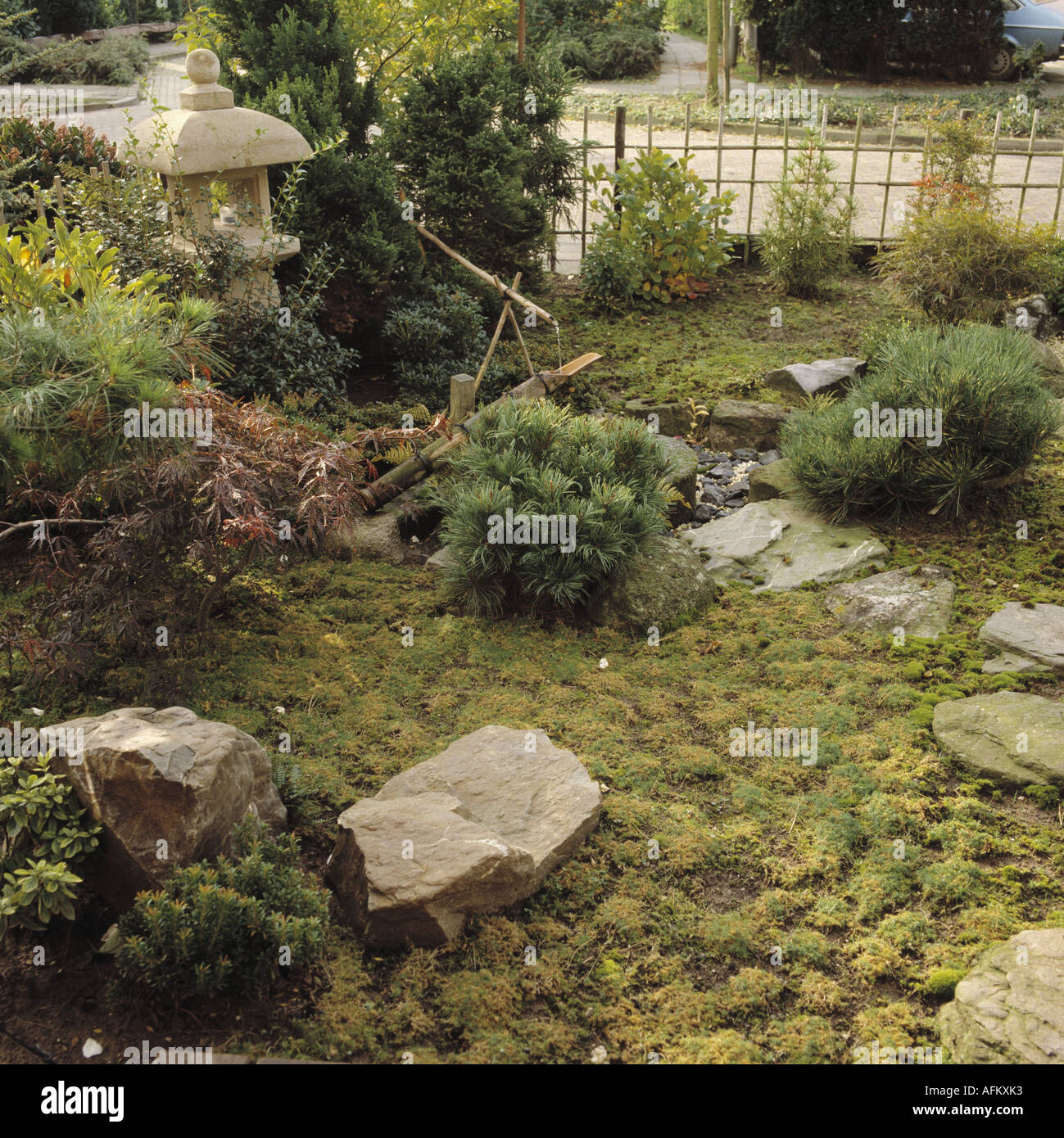 Große natürliche Felsen und kleinen Bambus Wasserspiel im orientalisch anmutenden Garten mit japanischen Steinlaterne und niedrigwüchsige Koniferen Stockfoto
