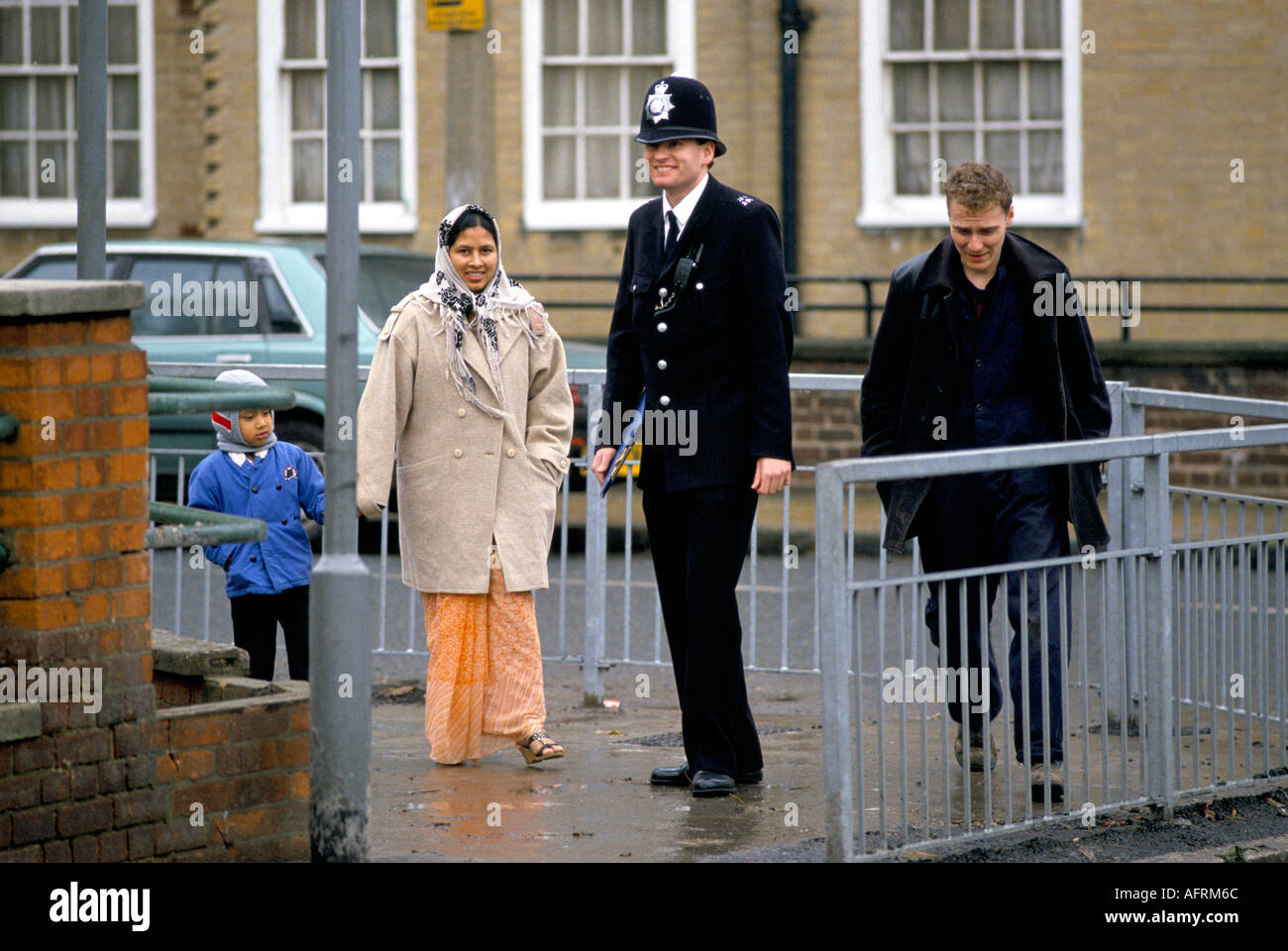 Polizist im Gespräch mit einer asiatischen Mutter und ihrem Kind. East London um 1995 UIK. 1990s. HOMER SYKES Stockfoto