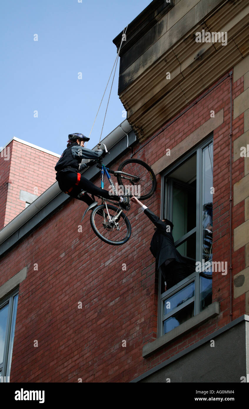 Mountain Bike Radfahrer Abseilen die Mauer eines Gebäudes mit Mann vom Bürofenster Stockfoto