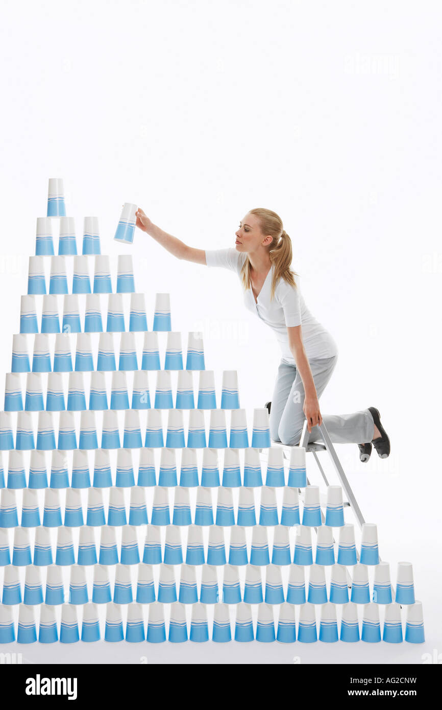 Frau kniend auf Leiter, Plastikbecher in Pyramide vor weißem Hintergrund zu stapeln Stockfoto