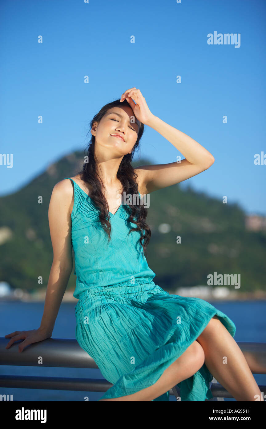 Junge Dame sitzt auf Geländer Zaun, Hand auf Stirn, Augen geschlossen Stockfoto