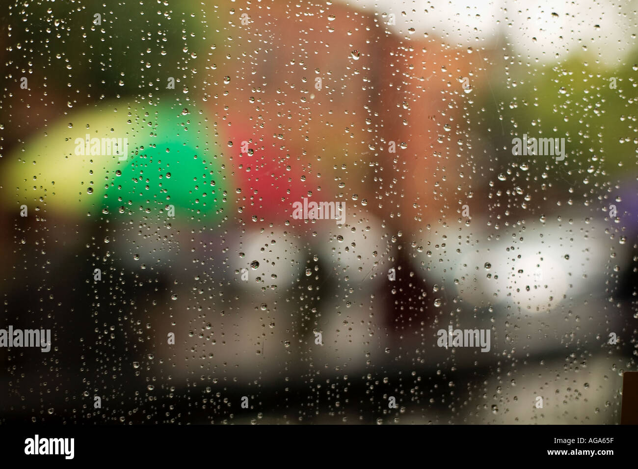 Regentropfen auf Restaurant-Fenster mit unscharfen Fokus Menschen tragen Regenschirme gehen auf der Straße jenseits Stockfoto