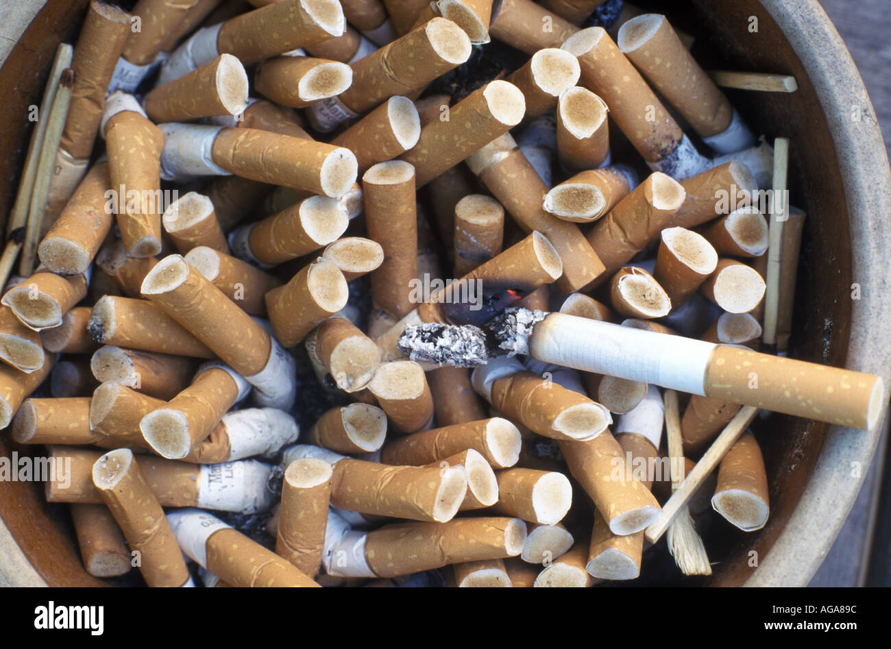 Eine Zigarette brennt auf einen Aschenbecher voller kippen. Stockfoto