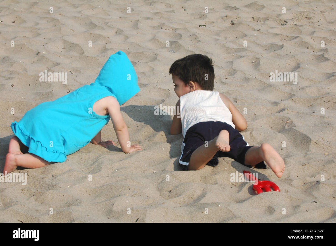 ein Babymädchen und Jungen spielen zusammen auf einem sandigen Strand im Sommer Stockfoto
