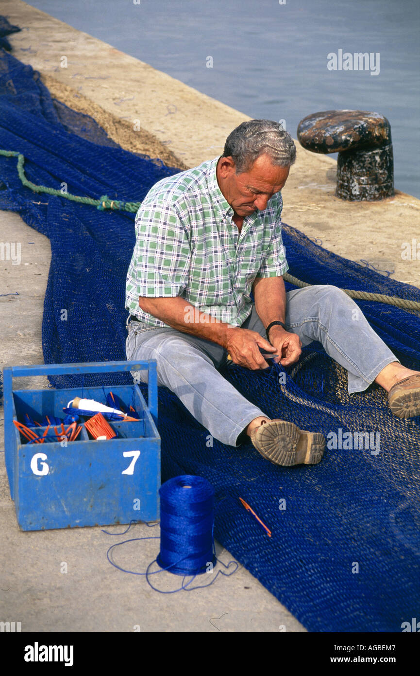 Ein einheimischer Fischer sitzt Reparatur seine Netze in der Sonne am Kai des Hafens von Santa Pola Stockfoto