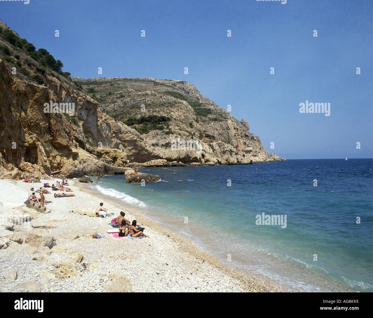 Eine kleine Anzahl von Urlaubern, die auf eines der kleinen einsamen Stränden sonnenbaden unterstützt durch schroffe Klippen und umspült von kristallklarem Wasser in Javea Stockfoto