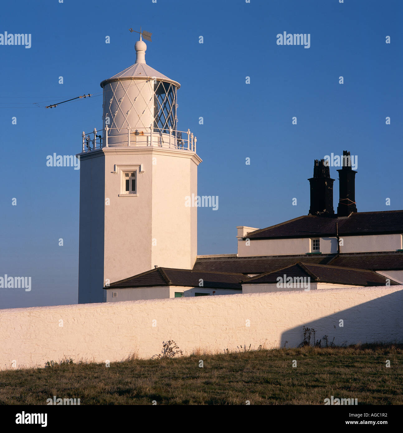 Ein großer weißer Leuchtturm an einem regelmäßigen weißen Haus mit krassen Zeilen auf dem schwarzen Dach befestigt Stockfoto