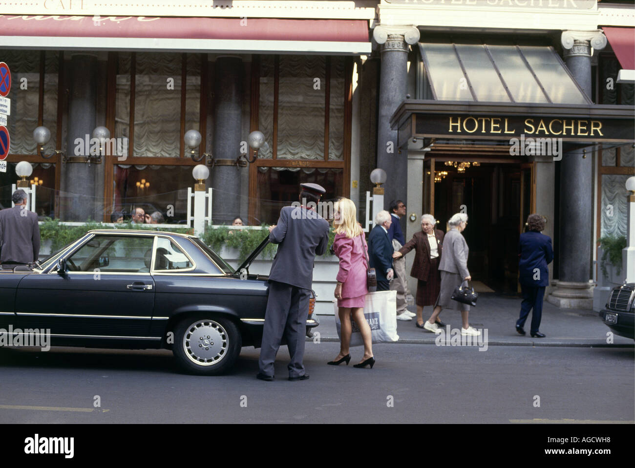 Besucher unter der Haube, die Schattierung der Eingang zum Hotel Sacher, während ein Chauffeur entlädt Einkäufe aus dem Kofferraum eines Autos für einen Hotel-s-Kunden Stockfoto